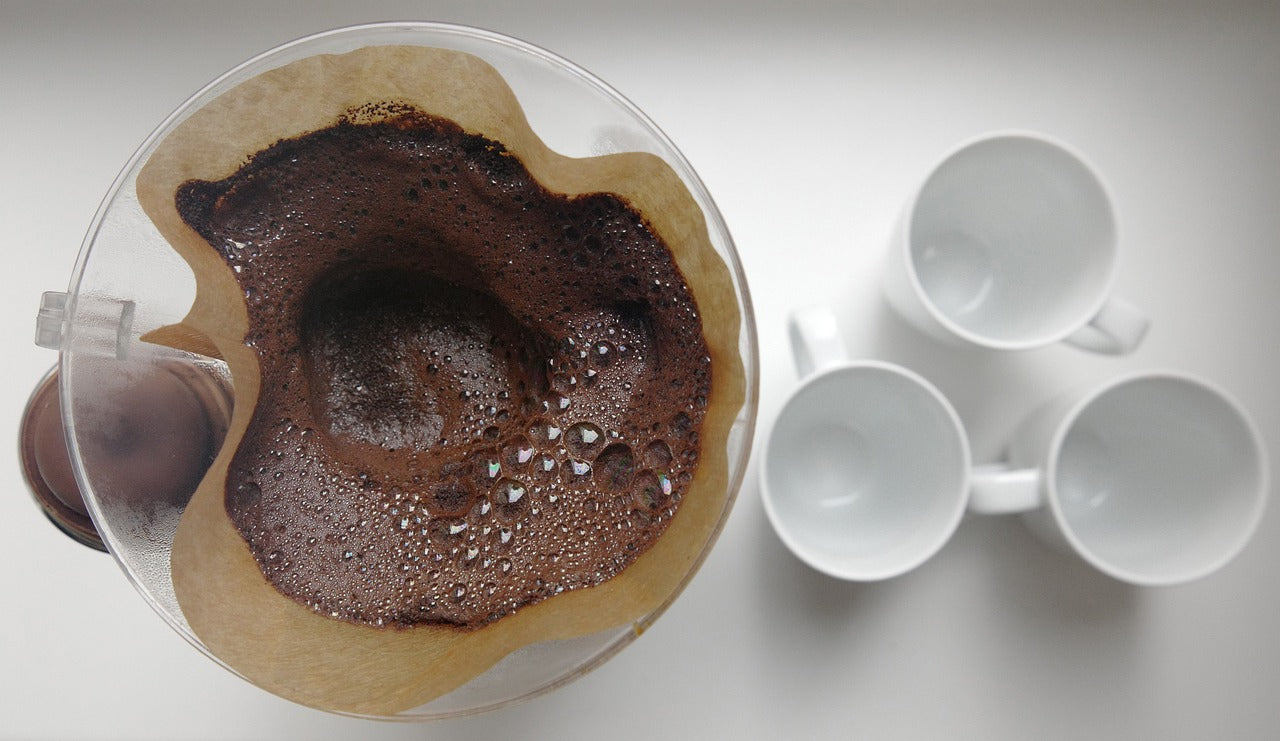 Kaffeefilter mit Kaffeesatz und drei Tasschen daneben